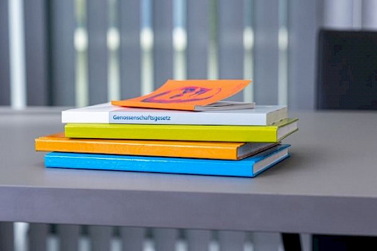 ein Bücherstapel in den Verbandsfarben blau, orange und grün